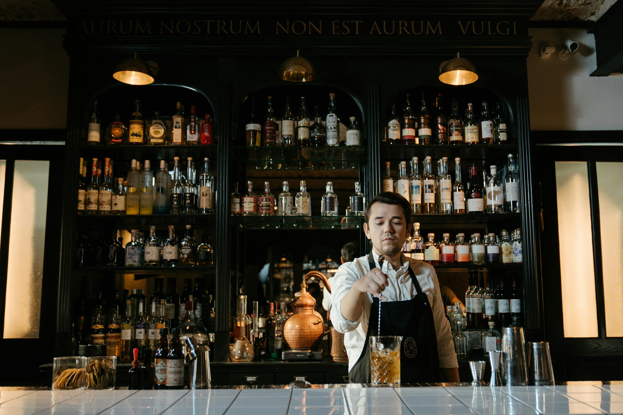 Bartender skillfully mixing a cocktail in a stylish bar with shelves of assorted bottles.